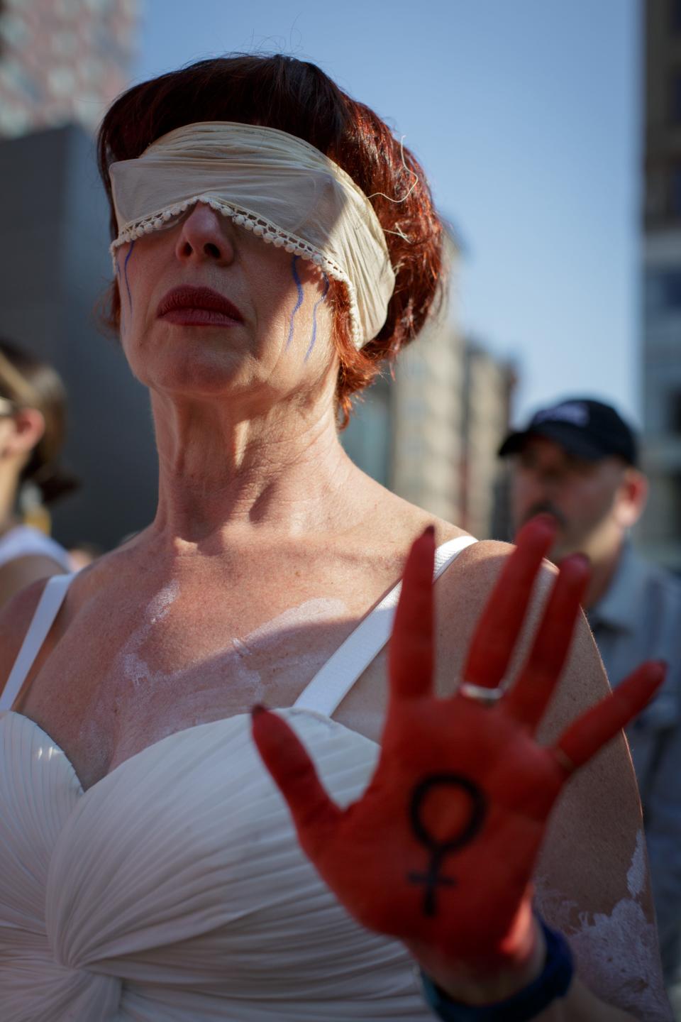 A woman wears a blindfold and displays her hand, painted red.