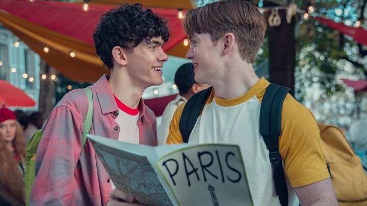 Two young men staring lovingly at one another looking at a pamphlet abbot Paris in a scene from Heartstopper.