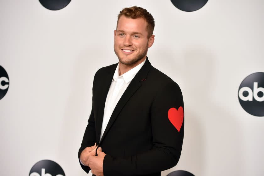Colton Underwood posing in black suit with a red heart on its arm