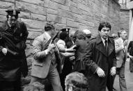 FILE - Secret Service agents and police officers swarm a gunman, obscured from view, after he attempted an assassination on President Ronald Reagan outside the Washington Hilton hotel on March 30, 1981. gan was shot and wounded by John Hinckley Jr. in an assassination attempt outside a Washington D.C. hotel. Reagan survived and eventually served two terms. (AP Photo/Ron Edmonds, File)