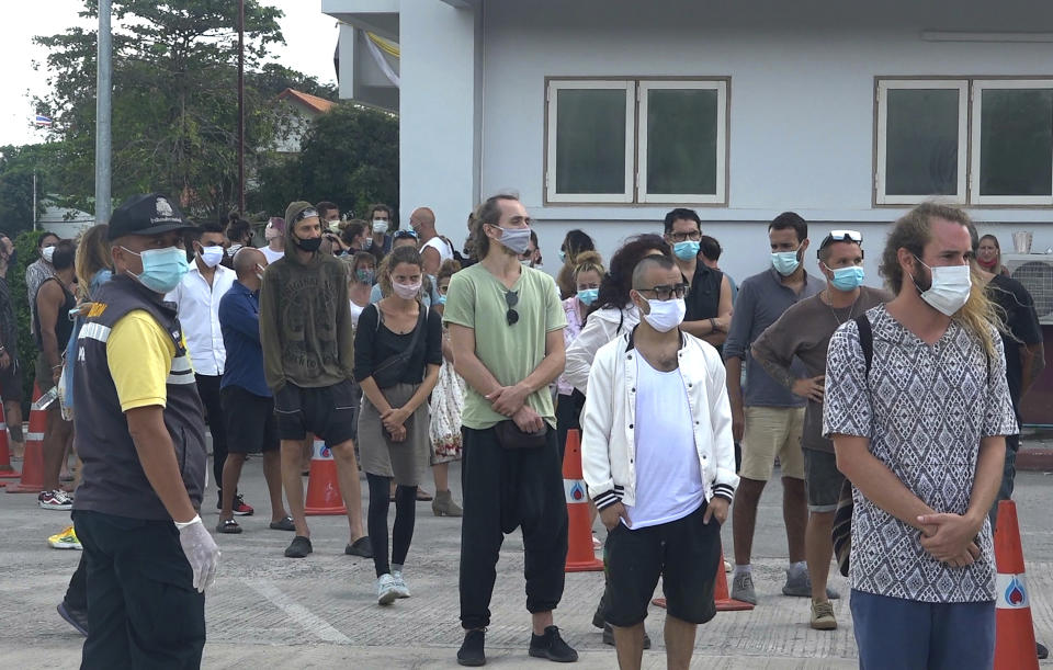 An immigration officer stand beside a group of foreigners in front of police station attending a court hearing through video conferencing on Koh Phangan island, Surat Thani province, southern Thailand, Thursday, Jan. 28, 2021. An illicit party in a bar on the popular island ended in a mass legal hangover on Thursday when a court handed out jail terms and fines to more than a hundred revelers for breaking national COVID restrictions. (AP Photo)