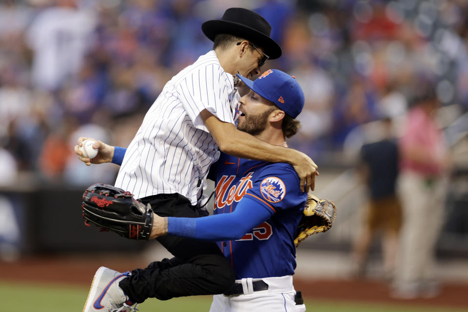 Musician Timmy Trumpet jumps into the arms of New York Mets' Tyler Naquin after throwing out a ceremonial first pitch before the Mets' baseball game against the Los Angeles Dodgers on Tuesday, Aug. 30, 2022, in New York. (AP Photo/Adam Hunger)