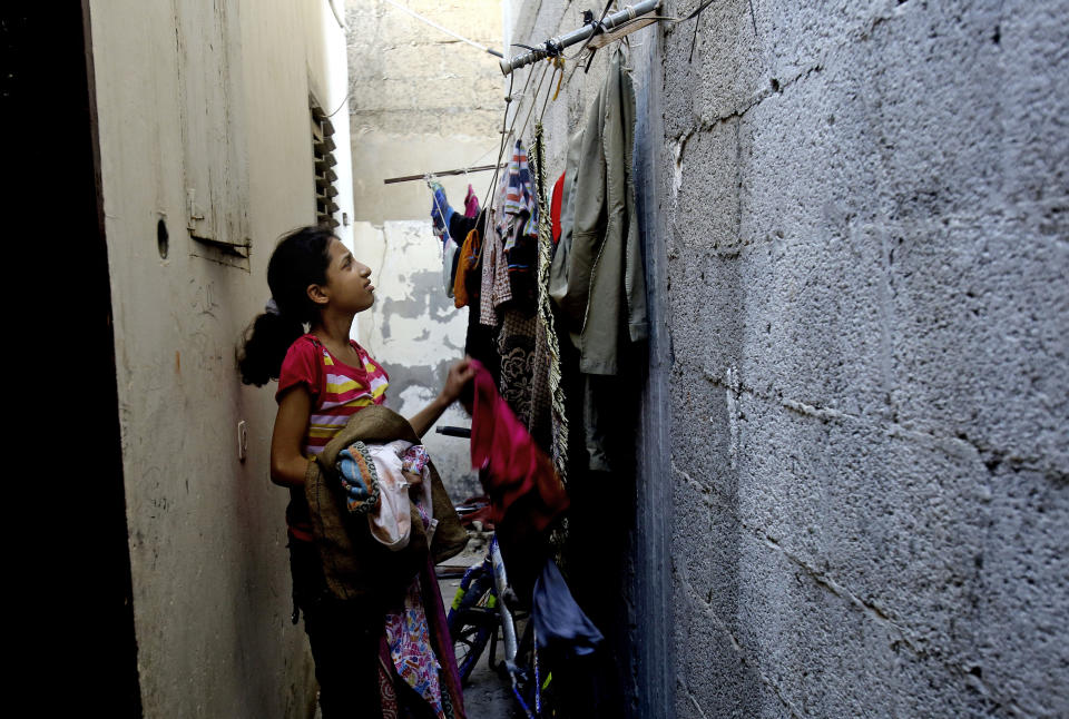 In this Monday, May 12, 2014 photo, Palestinian refugee, Aya Sattari,12, collects laundry at her family home in the Khan Younis Refugee Camp, in the southern Gaza Strip. As Palestinians mark the Nakba’s 66th anniversary Thursday, May 15, 2014 the Palestinian refugee crisis has transitioned from temporary to seemingly permanent. Tent camps of the 1950s have turned into urban slums with some alleys so narrow residents can only walk single file past drab multi-story buildings. (AP Photo/Adel Hana)