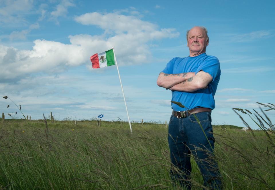 Michael Forbes poses for a photograph beside the Mexican flag he erected alongside Donald Trump's International Golf Links course, north of Aberdeen on the East coast of Scotland, on June 21, 2016. Trump is heading to Scotland to relaunch his Turnberry golf course and hotel in southwest Scotland following a £200 million ($300 million, 260 million euro) revamp of the resort, and the property tycoon will also visit his Balmedie course. Another Mexican flag is being flown at the nearby home of Michael Forbes, who refused to sell his land to Trump before the course opened.  / AFP / Michal Wachucik        (Photo credit should read MICHAL WACHUCIK/AFP via Getty Images)