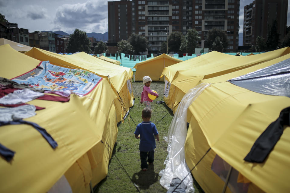 Children walk in a camp built for homeless Venezuelan migrants in Bogota, Colombia, Wednesday, Nov. 21, 2018. The camp was built by the city's social welfare secretary to accommodate migrants who had previously been living in tents made of plastic sheets and scrap materials outside the city's bus terminal. (AP Photo/Ivan Valencia)