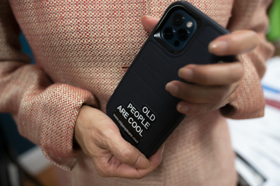 Tina Sandri, CEO of Forest Hills of DC senior living facility, displays her phone decorated with a sticker reading "Old people are cool," while working in her office on Thursday, Dec. 8, 2022, in Washington. Coronavirus-related hospital admissions are climbing again in the United States, with older adults a growing share of U.S. deaths and less than half of nursing home residents up to date on COVID-19 vaccinations. (AP Photo/Nathan Howard)