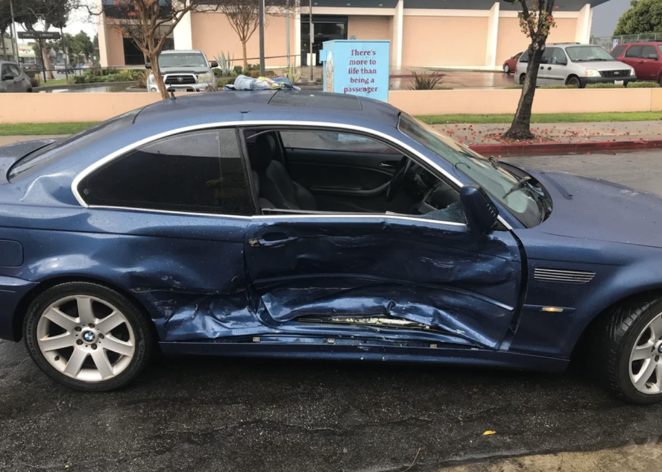 Blue car with damaged passenger side door and side panel, parked on a wet street