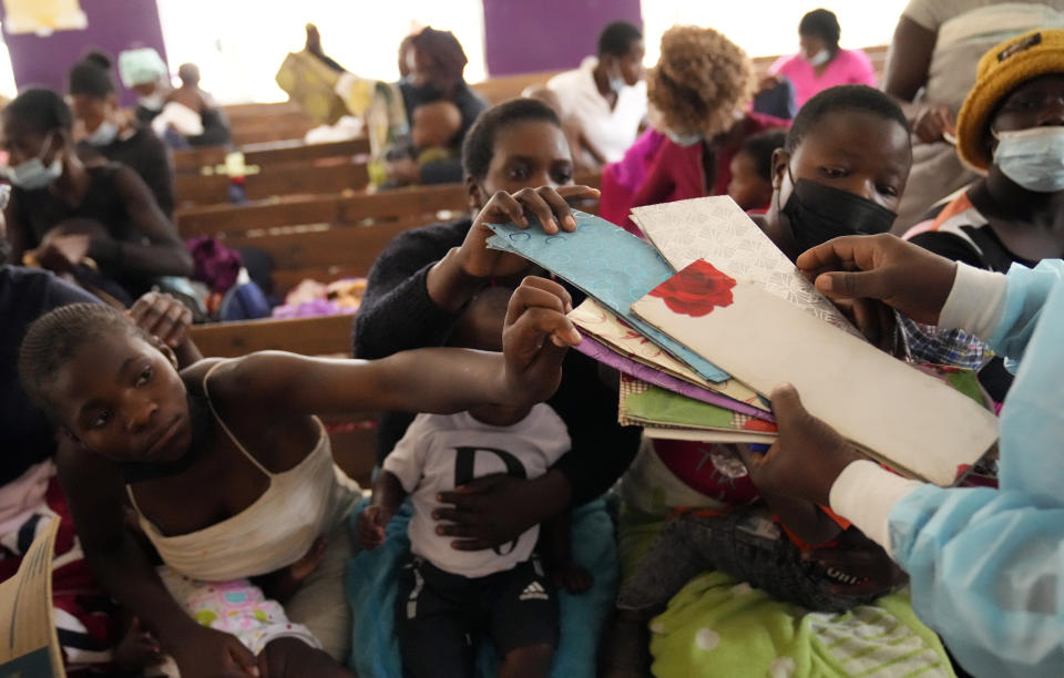 Women holding babies have their health cards inspected by a nurse while seated on wooden benches at a clinic in Harare, Zimbabwe, Thursday, Sept. 15, 2022. Church members in Zimbabwe are getting their children vaccinated against measles in secret amid a deadly outbreak. It's to avoid being shunned by religious leaders who are opposed to modern medicine. (AP Photo/Tsvangirayi Mukwazhi)