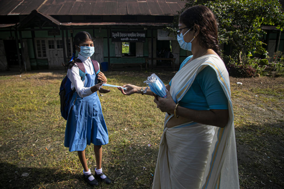 A school principal distributes masks to students as schools in north-eastern Assam state reopen after being closed for months due to the coronavirus pandemic in Gauhati, India, Monday, Nov. 2, 2020. (AP Photo/Anupam Nath)