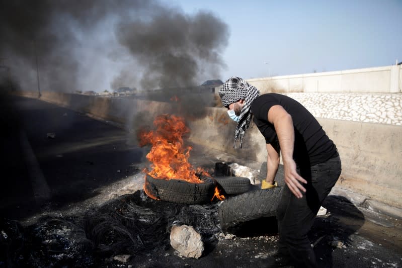 A demonstrator pulls a tire next to burning barricade at the highway during ongoing anti-government protests at Nahr El Kalb