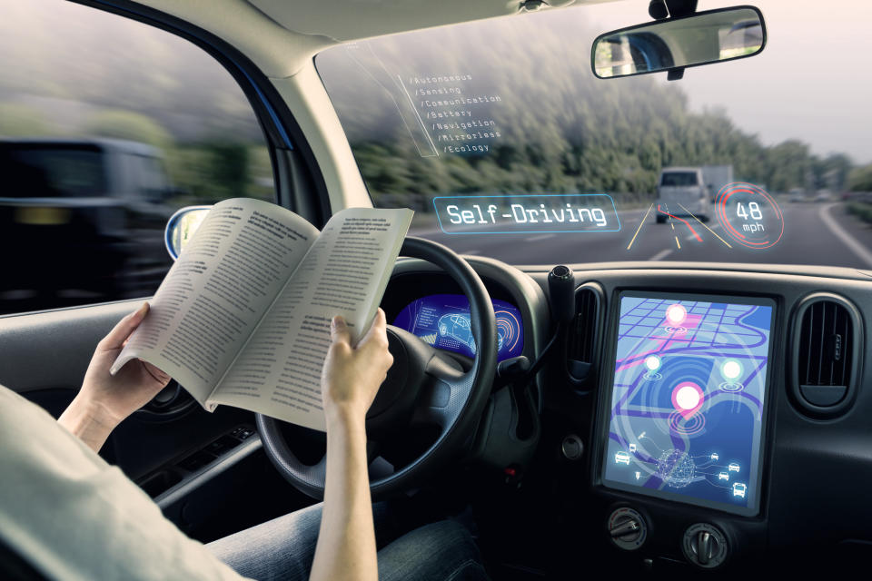 An illustrated view of the interior of a self-driving car. A woman sits reading while the car drives itself on a highway.