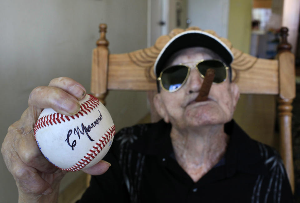 In this April 23, 2013 photo, Cuba's former pitcher Conrado Marrero, the world's oldest living former major league baseball player, holds up a baseball with his signature at his home, two days before is 102nd birthday, as he holds an unlit cigar in his mouth in Havana, Cuba. In addition to his longevity, the former Washington Senator has much to celebrate this year. After a long wait, he finally received a $20,000 payout from Major League baseball granted to old-timers who played between 1947 and 1979. The money had been held up since 2011 due to issues surrounding the 51-year-old U.S. embargo on Cuba, which prohibits most bank transfers to the Communist-run island. But the payout finally arrived in two parts, one at the end of last year, and the second a few months ago, according to Marrero's family. (AP Photo/Franklin Reyes)