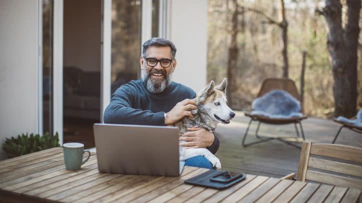 A man looks over his retirement portfolio while sitting on his deck with his dog. 