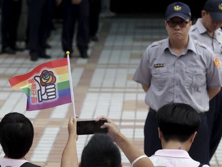 A participant takes a picture of a rainbow flag while a police officer stands guard during a rally demanding the Taiwanese government legalize same-sex marriage in front of the ruling Nationalist Kuomintang Party headquarters in Taipei, Taiwan, July 11, 2015. REUTERS/Pichi Chuang