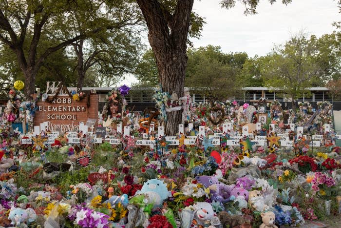 Stuffed animals, flowers, wreaths, and other decorations sit among crosses with victims' names on them