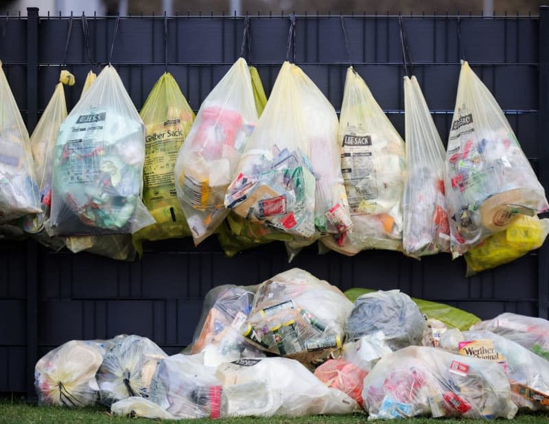 Yellow bags of plastic waste and packaging waste hang on a fence in front of an apartment building. Christian Charisius/dpa