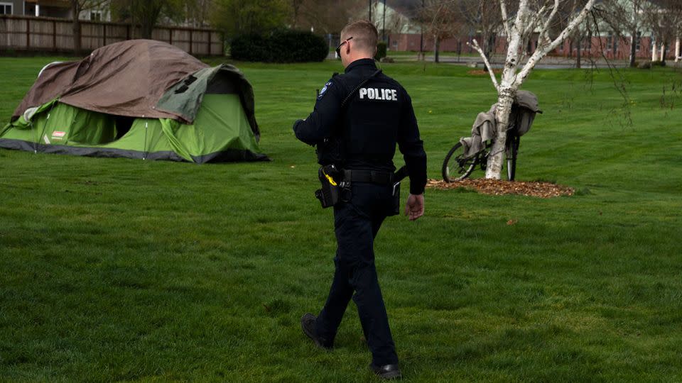 A Grants Pass police officer checks on a homeless person after relatives asked for a welfare check at Fruitdale Park on March 23, 2024. - Jenny Kane/AP/File