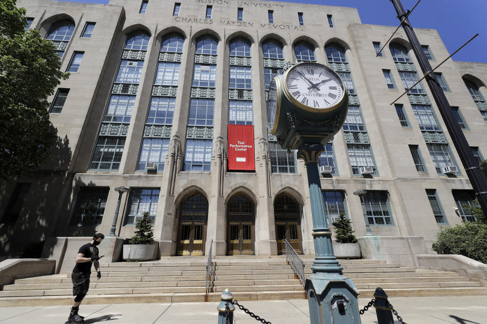 In this Wednesday, May 20, 2020 photo a passer-by skates past an entrance to the Tsai Performance Center on the campus of Boston University, in Boston. Boston University is among a growing number of universities making plans to bring students back to campus this fall, but with new measures meant to keep the coronavirus at bay. (AP Photo/Steven Senne)