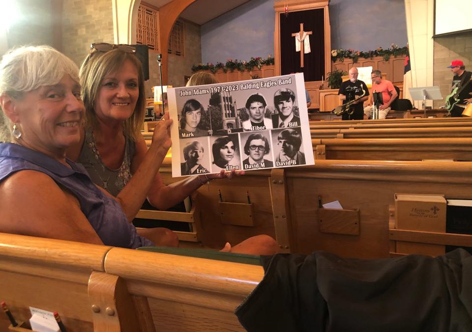 Judy Miller and Patti Milliken Spice hold the high school photos of the Balding Eagle Band, which is rehearsing in the background. Miller and Spice are 1973 graduates from Adams High, as are most of the band members.