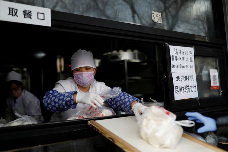 FILE PHOTO: Employee deliver buns to a customer through a ramp from the restaurant counter at a store, as the country is hit by an outbreak of the novel coronavirus, in Beijing