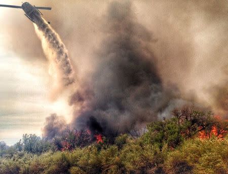 A helicopter makes a drop on a fire which broke out in Arizona and spread into California, sparking the evacuation of two recreational vehicle parks near the Havasu National Wildlife Refuge in California in this April 6, 2016 handout photo provided by San Bernardino County Fire Department via Twitter. REUTERS/San Bernardino County Fire Department via Twitter/Handout via Reuters