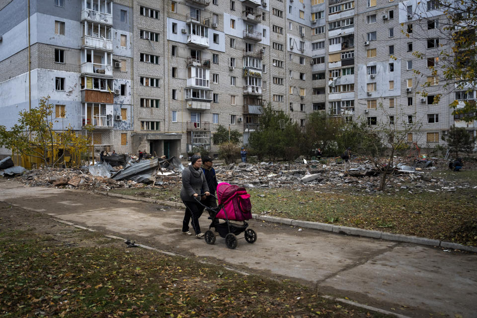 A couple pushing a baby stroller walks past a building damaged by a Russian missile in Mykolaiv, Sunday, Oct. 23, 2022. (AP Photo/Emilio Morenatti)