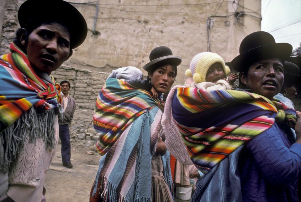 A group of Aymaran women with babies on their backs looking behind them.