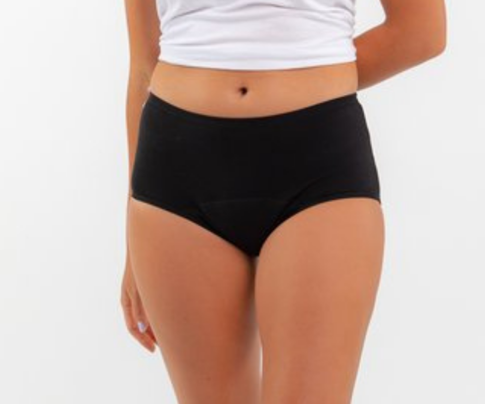 Caucasian girl wears black mid-rise Eco Orgaknix period undies with a white crop tshirt.