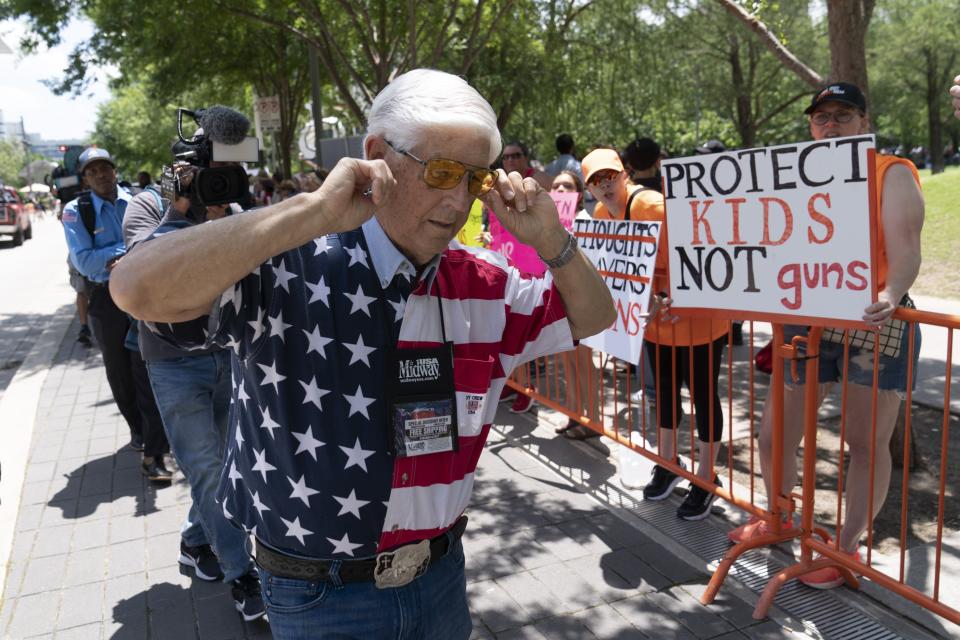 A member of the National Rifle Association plugs his ears with his fingers as he walks past protesters during the NRA's annual meeting at the George R. Brown Convention Center in Houston, Friday, May 27, 2022. (AP Photo/Jae C. Hong)