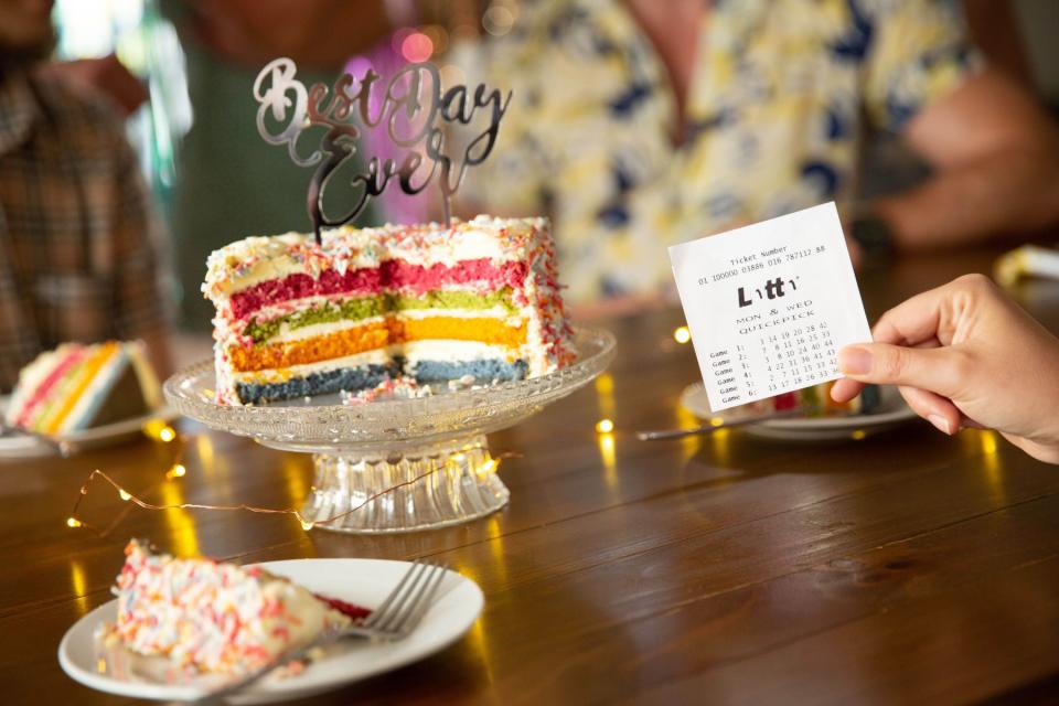 Lotto ticket held beside rainbow layer cake, with sign on top reading 