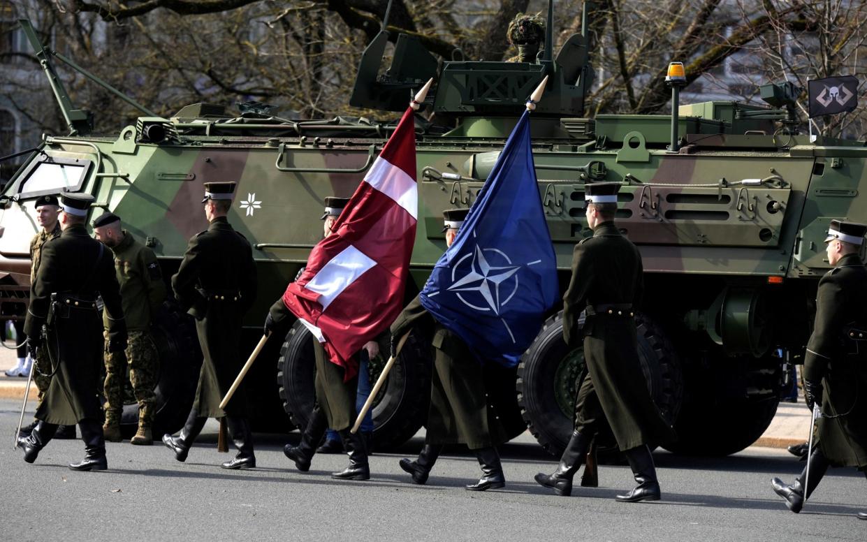 Latvian army servicemen hold Latvian and Nato flags as Latvia celebrates the anniversary of joining the alliance in Riga, Latvia March 28, 2024