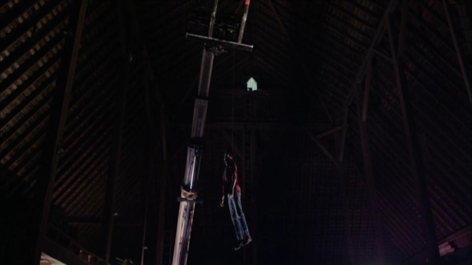 A man's dead body hangs from a crane by a rope