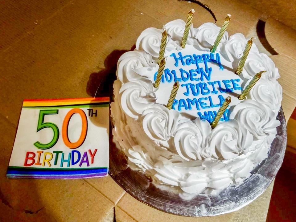 A white cake with blue text and a 50th Birthday napkin on a carboard box