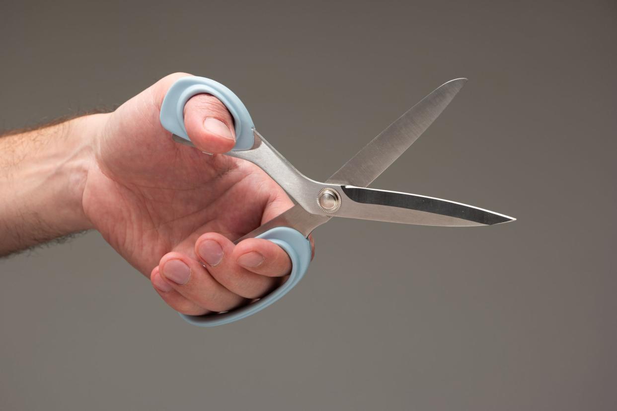 Male left hand holding a grey-rimmed pair of left-handed scissors against a grey gradient background