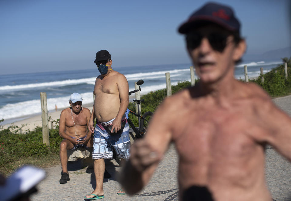 People, one wearing a mask, rest and exercise along the seafront next to Barra de Tijuca beach, as Fernando Ferreira, right, speaks during an interview as he takes a walk outside amid the new coronavirus pandemic in Rio de Janeiro, Brazil, Wednesday, April 29, 2020. The retired dentist and lawyer recommended reading the Bible and Albert Camus’ The Plague, citing them as evidence pandemics have always happened to some degree, and said restrictions on commerce are “absurd.” (AP Photo/Silvia Izquierdo)