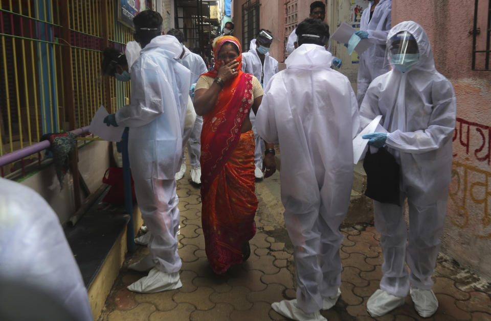 A woman covers her face as she walks past health workers arriving to administer a free medical checkup in a slum in Mumbai, India, Sunday, June 28, 2020. India is the fourth hardest-hit country by the COVID-19 pandemic in the world after the U.S., Russia and Brazil. (AP Photo/Rafiq Maqbool)