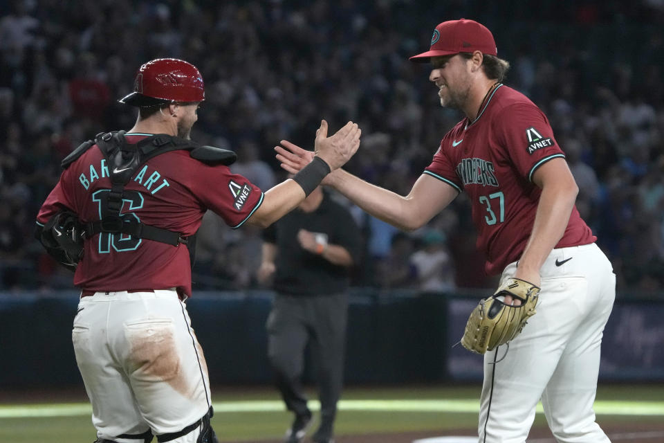 Arizona Diamondbacks catcher Tucker Barnhart, left, and pitcher Kevin Ginkel (37) celebrate after defeating the Colorado Rockies in a baseball game, Sunday, March 31, 2024, in Phoenix. (AP Photo/Rick Scuteri)