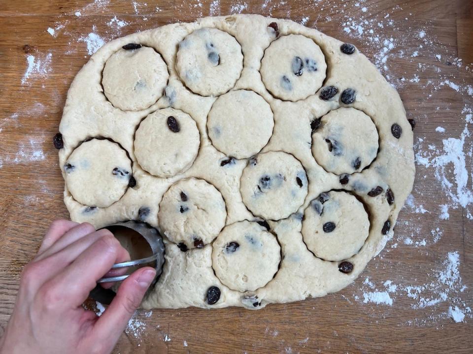 An overhead shot shows a woman's hand using a fluted cookie cutter to make circles out of rolled-out dough.