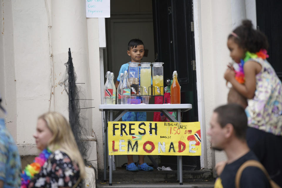 A child sells homemade drinks from a doorway, during the Children's Day Parade, part of the Notting Hill Carnival celebration in west London, Sunday, Aug. 27, 2023. (Yui Mok/PA via AP)