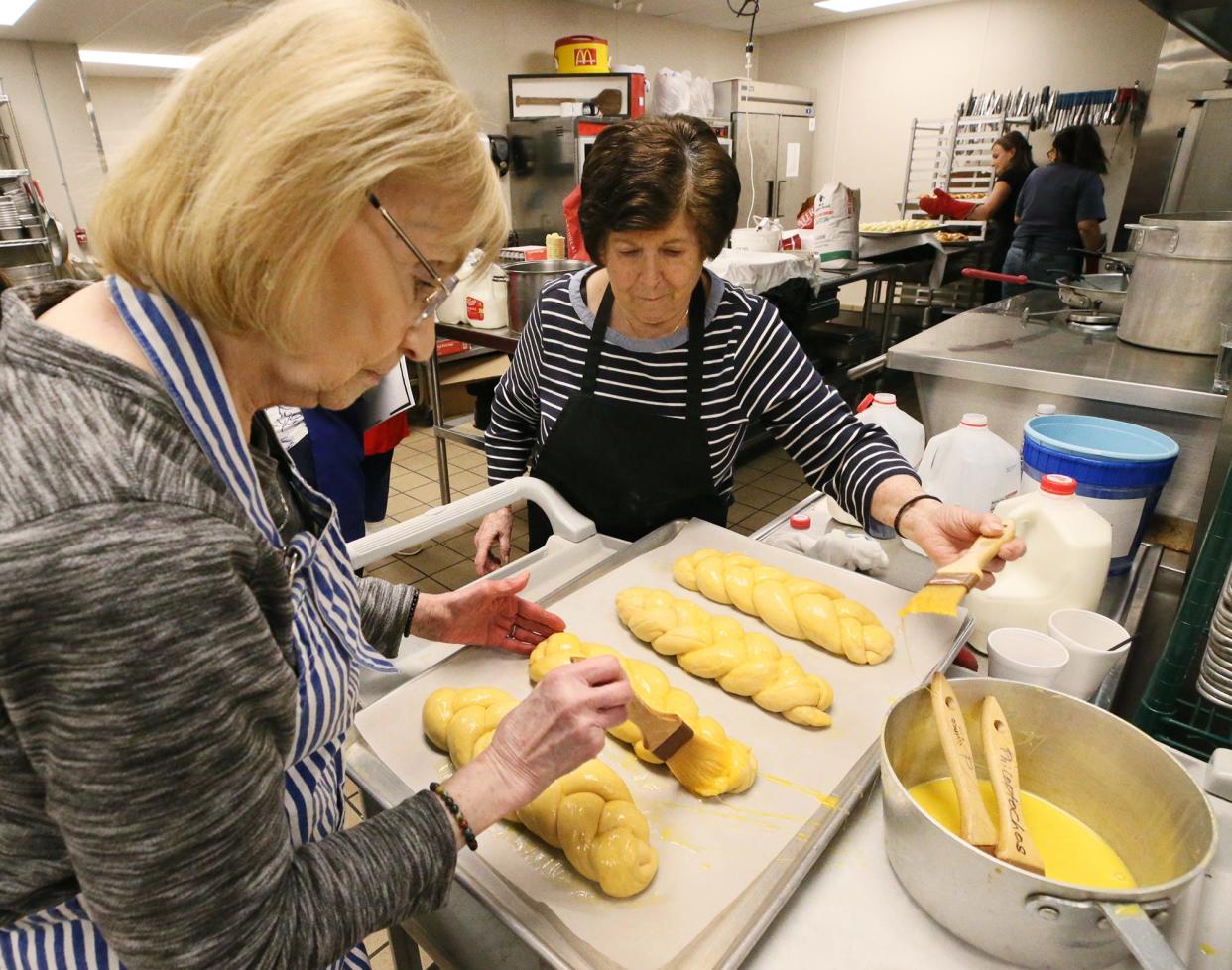 Maria Moore and Eleni Kardoulias wash tsourekia with egg Tuesday with volunteer bakers from Annunciation's Philoptochos Society and the Kalymnian Society of Campbell, Ohio. The Greek Easter bread will be sold at Annunciation's Easter Bake Sale March 27 and 28.
