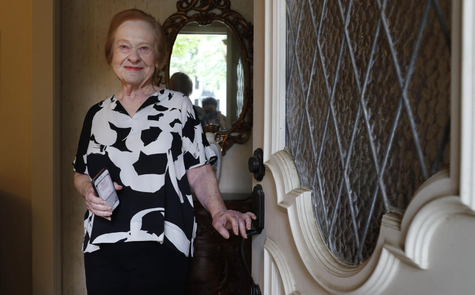 Dell Kaplan, 81, smiles for a photo in the doorway of her home in Plano, Texas Friday, May 15, 2020. For Kaplan, the offer to get calls from a stranger just to chat while staying home during the coronavirus pandemic was immediately appealing. "It gets pretty lonely here by yourself," said Kaplan, a suburban Dallas resident who has been missing meals out with friends, family get-togethers and going to classes at a nearby college. The program being offered by the city of Plano is among those that have popped up across the U.S. during the pandemic to help older adults with a simple offer to engage in small talk. (AP Photo/LM Otero)