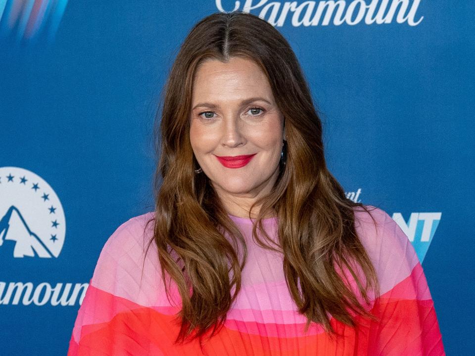 Drew smiling in a red and pink dress in front of a backdrop.