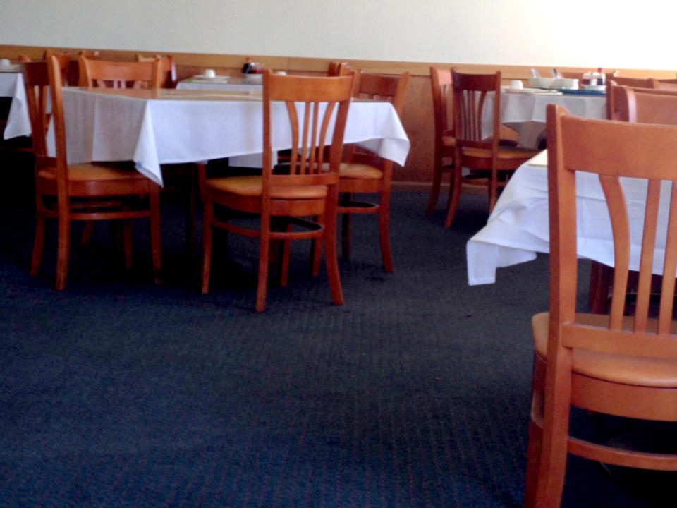 An empty restaurant with wooden chairs and tables set with white tablecloths