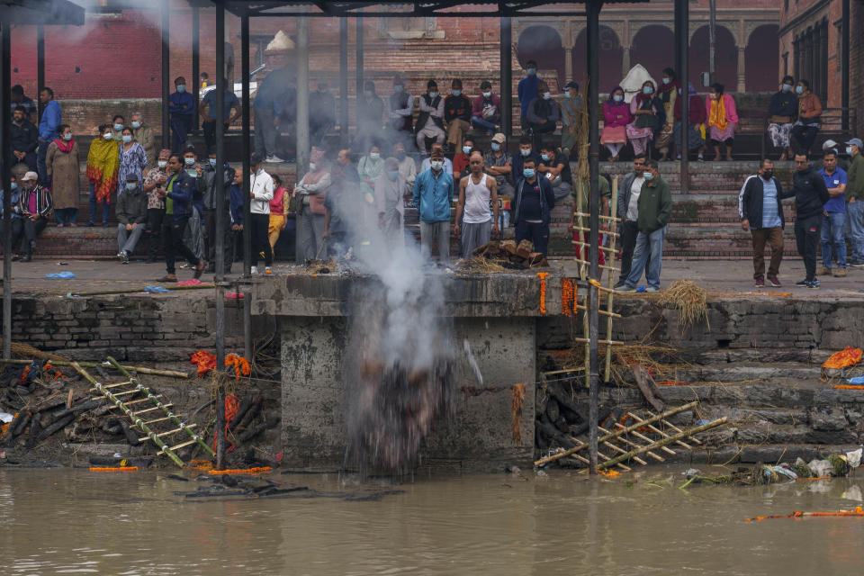 Un hombre empuja unos restos cremados al río Bagmati en el templo de Pashupatinath, en Katmandú, Nepal, el sábado 28 de mayo de 2022. El templo fue declarado Patrimonio de la Humanidad por UNESCO en 1979. (AP Foto/Niranjan Shrestha)