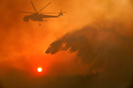 A firefighting helicopter makes water drop as a wildfire burns near the village of Metochi, north of Athens, Greece. REUTERS/Giorgos Moutafis