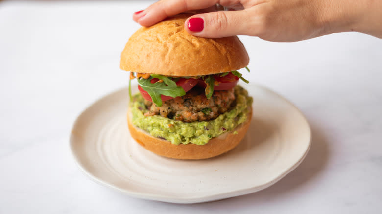 hand on top of salmon burger with guacamole on plate