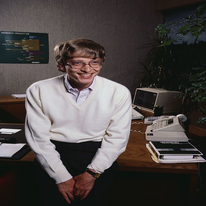 Bill Gates sitting on a desk with in early '80s technology