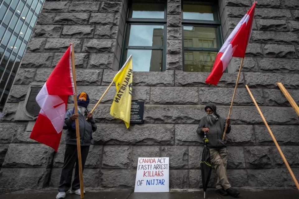 two men stand with canadian and khalistan flags and a sign that says ‘canada, act fast, arrest killers of nijjar’