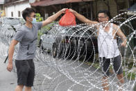 A man collect supplies over barbed wire in the coronavirus locked down area of Selayang Baru, outside of Kuala Lumpur, Malaysia, on Sunday, April 26, 2020. The lockdown was implemented to allow authorities to carry out screenings to help curb the spread of coronavirus. (AP Photo/Vincent Thian)