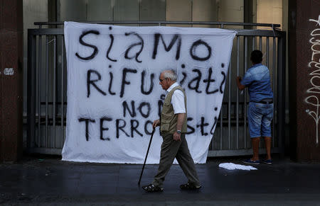 A man walks as a refugee hangs a banner reading "We are refugees, we aren't terrorists", after being forcibly removed from a building where they had been living, in central Rome, Italy, August 20, 2017. REUTERS/Alessandro Bianchi